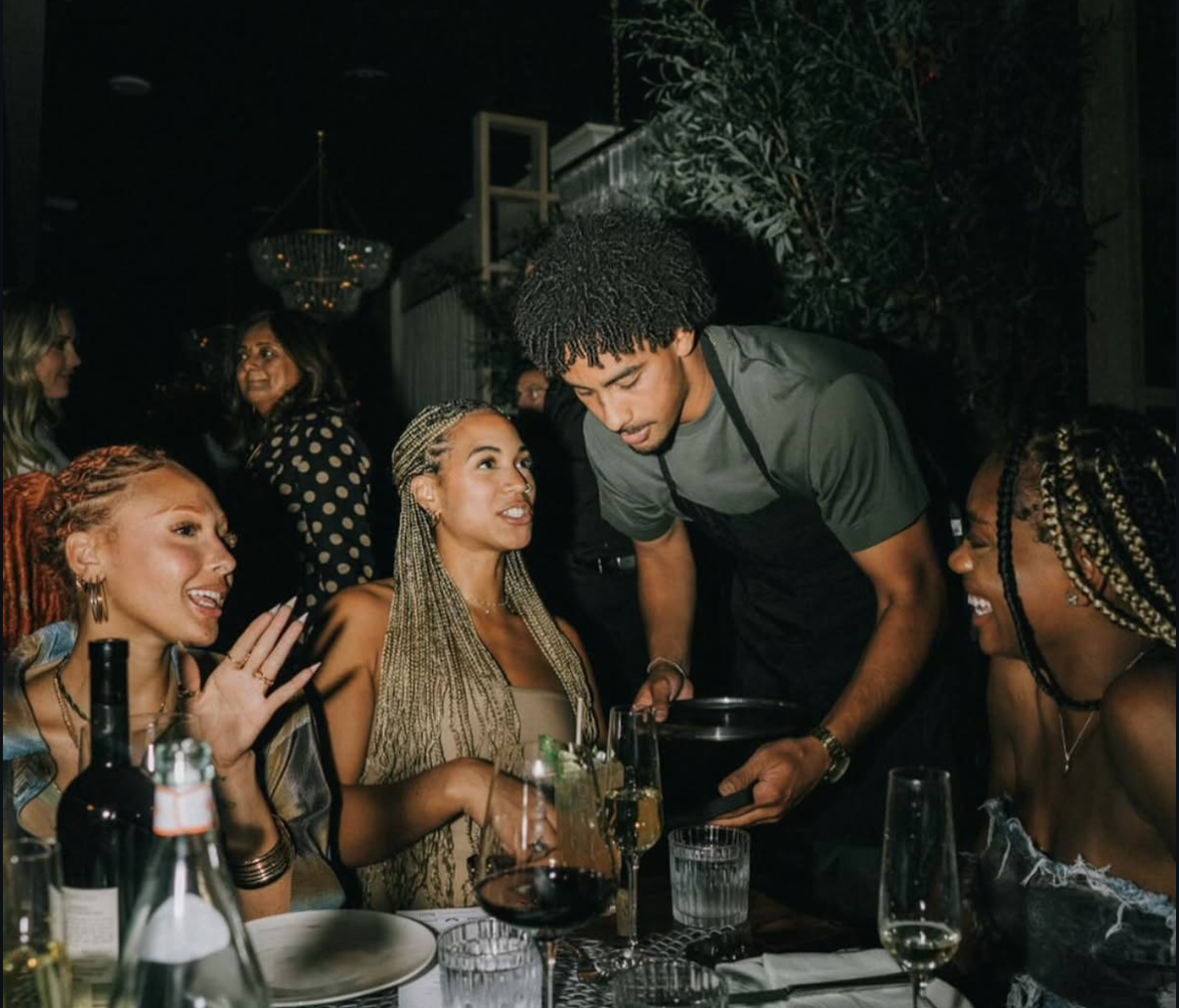 Celebrity waiter serving a table of laughing guests.
