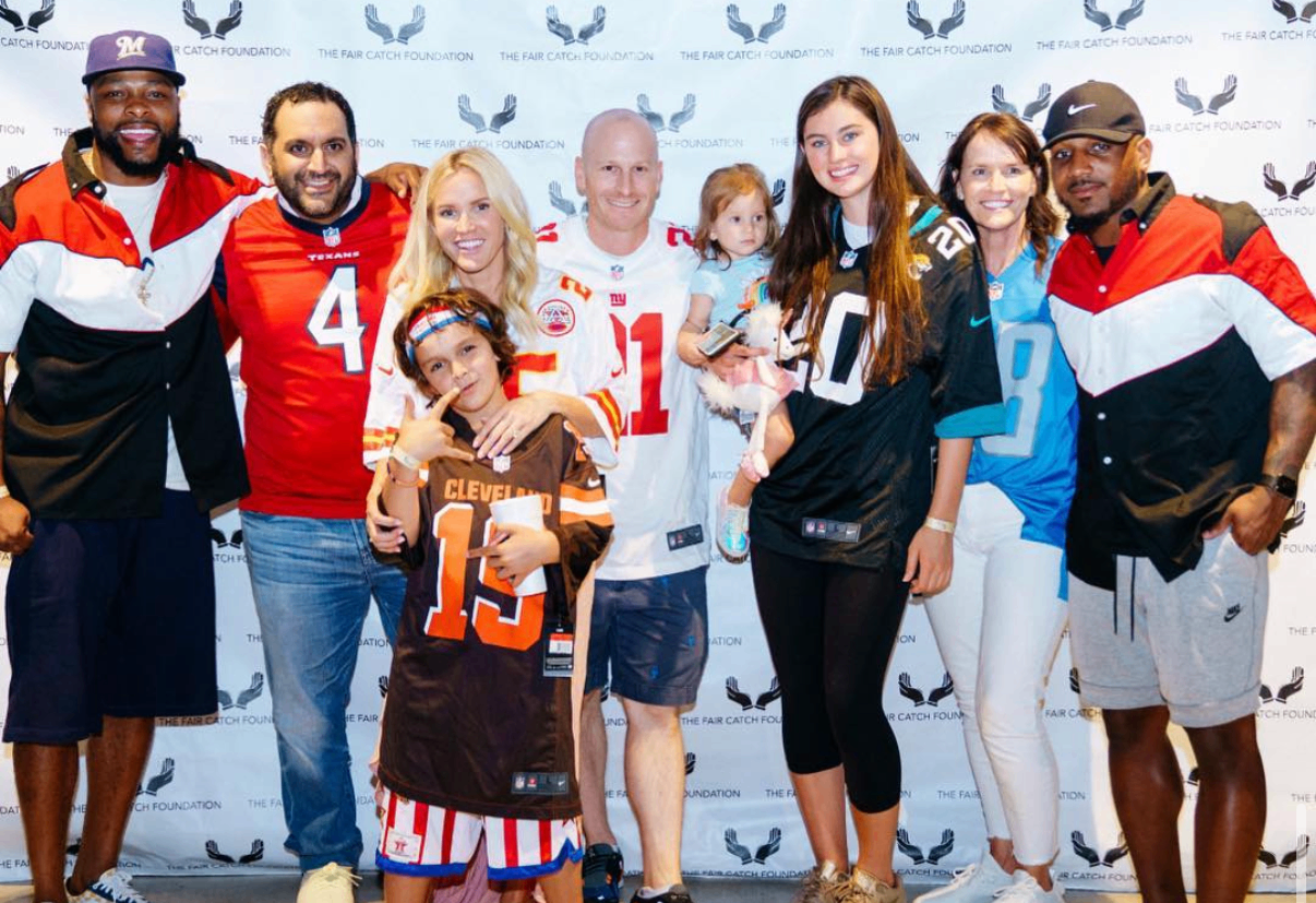 A group of guests and celebrities in jerseys pose together with a young fan at the 2018 Bowl with the Pros Charity Event.