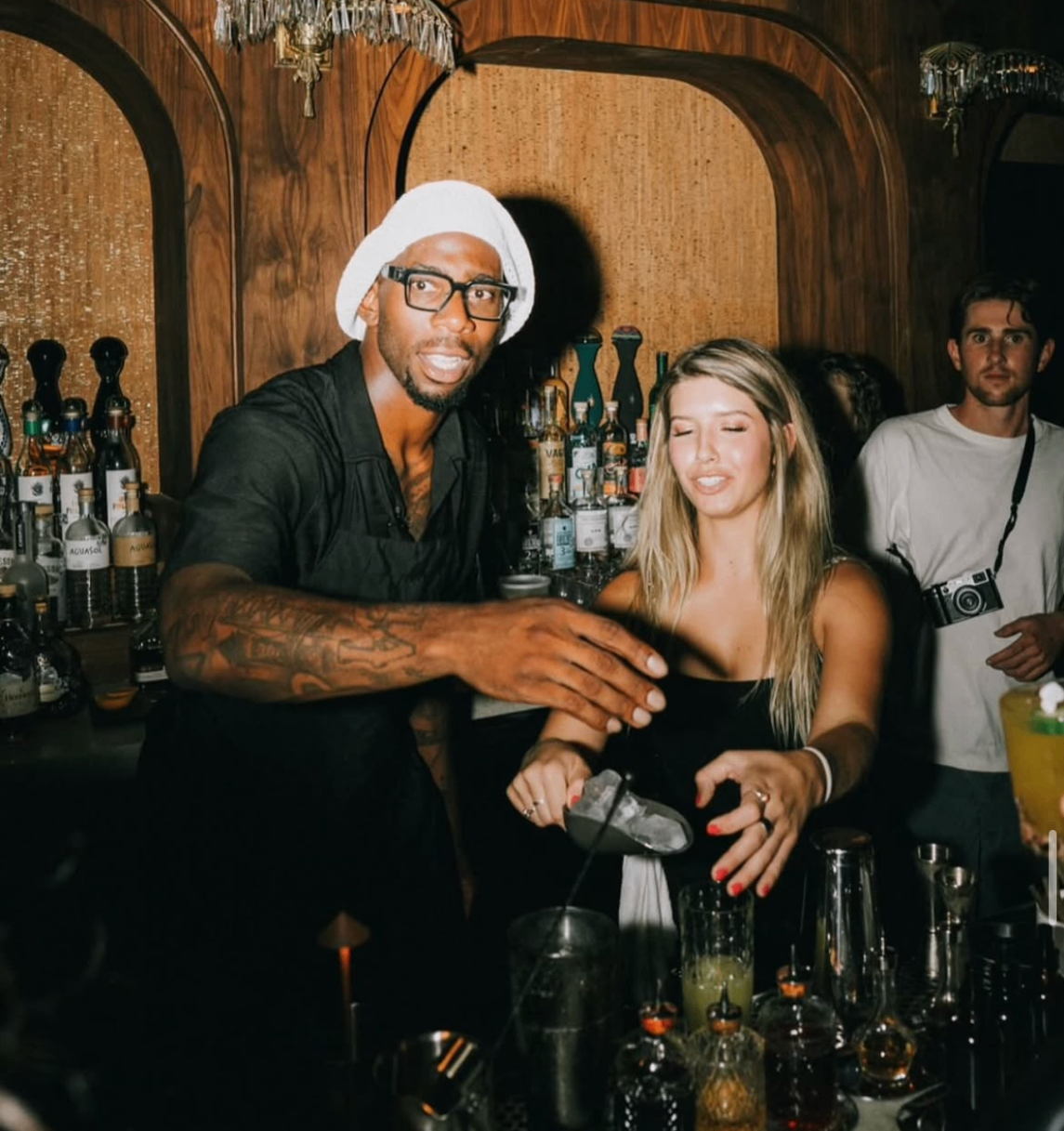 A celebrity waiter mixes cocktails with a guest behind the bar during the 2024 event.