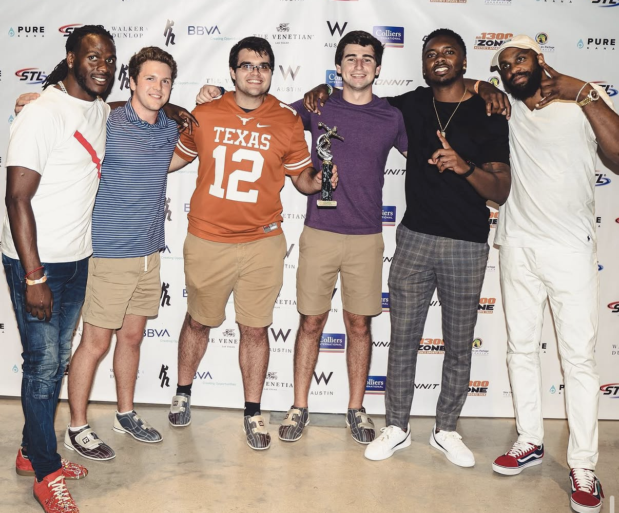A group of guests and celebrity players pose with a trophy in front of the sponsor step-and-repeat at the 2019 Bowl with the Pros Charity Event.