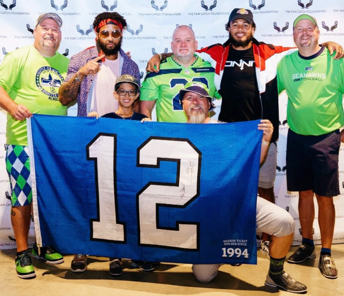 A group of Seahawks fans and celebrity guests pose with a signed number 12 flag at the 2018 Bowl with the Pros Charity Event.