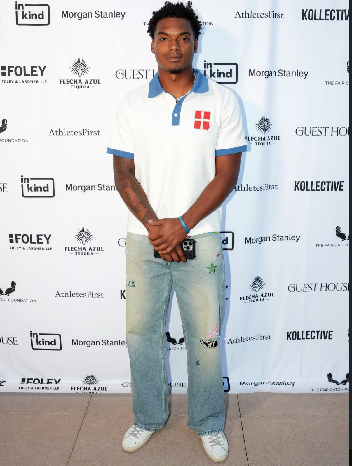 A guest in a white and blue polo poses in front of the 2025 sponsor step-and-repeat.