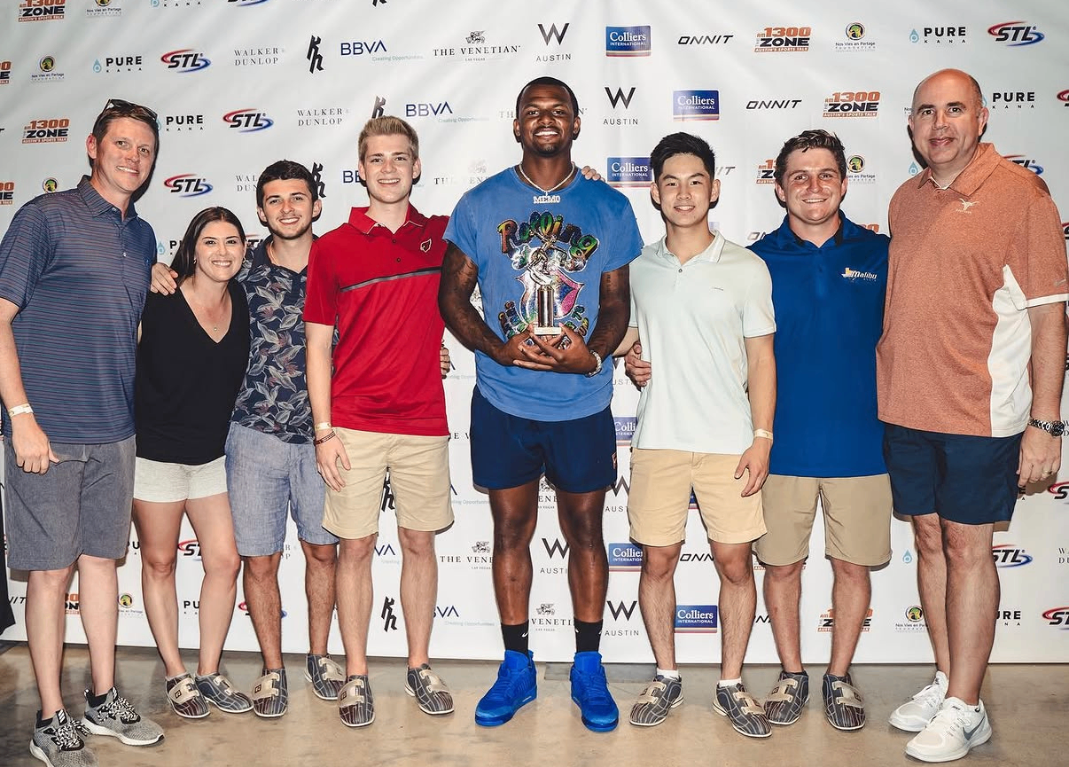 A celebrity guest holds a trophy while posing with supporters on the sponsor backdrop at the 2019 Bowl with the Pros Charity Event.
