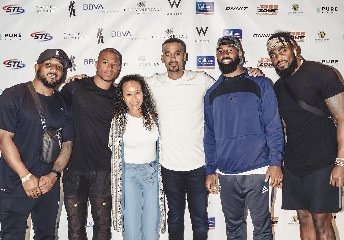 A group of celebrity players and a guest pose together for a photo on the sponsor backdrop at the 2019 Bowl with the Pros Charity Event.