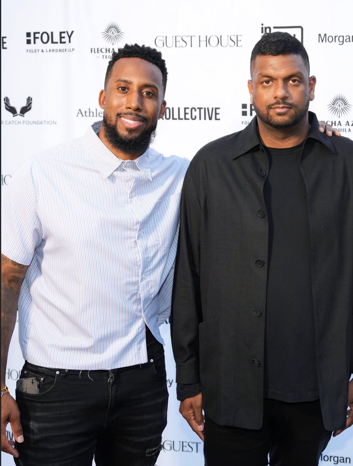 Two guests pose together in front of the sponsor wall at the 2026 Celebrity Waiter Night.