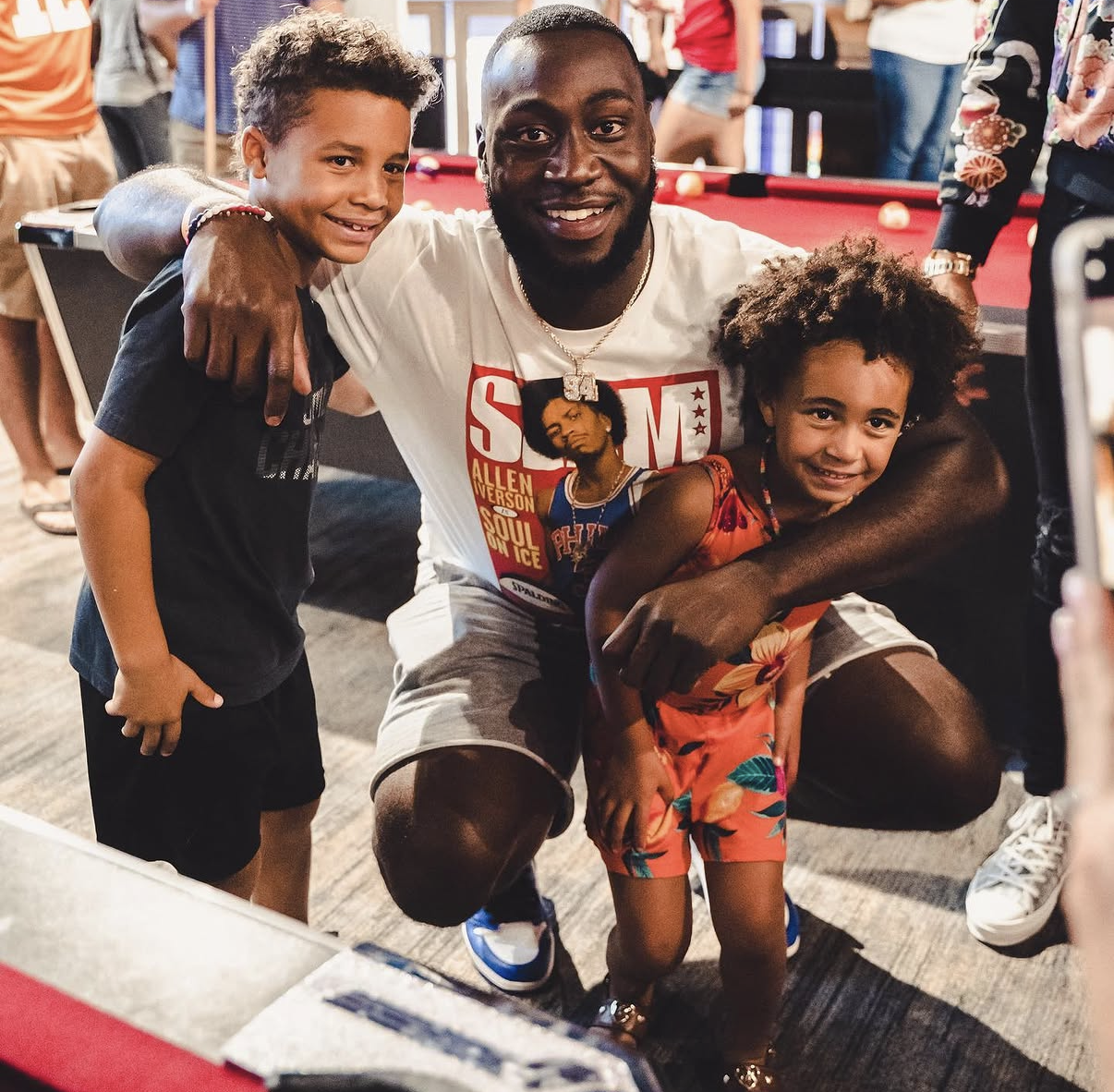 A celebrity player kneels down to pose with two young fans at the 2019 Bowl with the Pros Charity Event.
