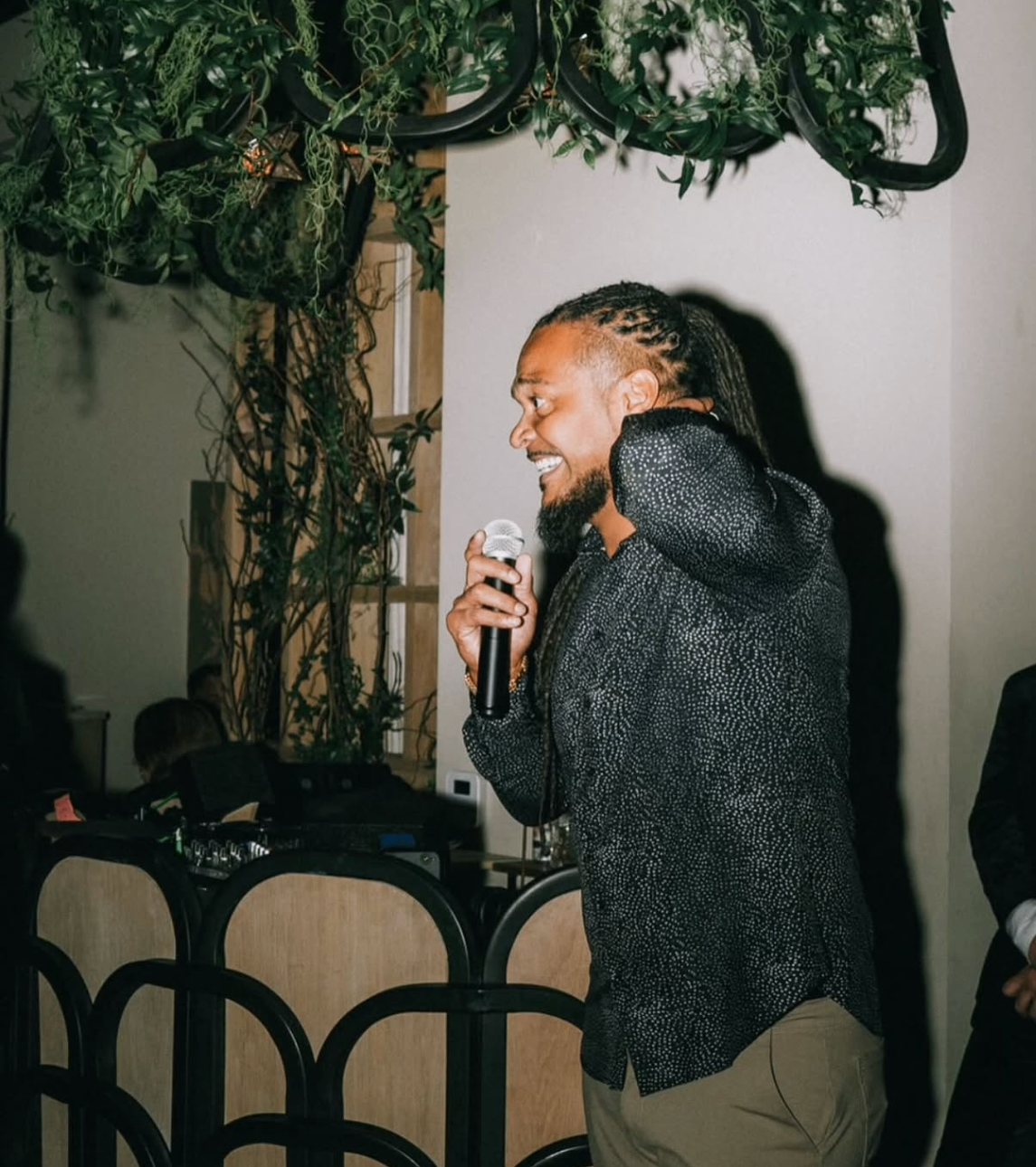 Celebrity waiter sings on the microphone under greenery-draped chandeliers.
