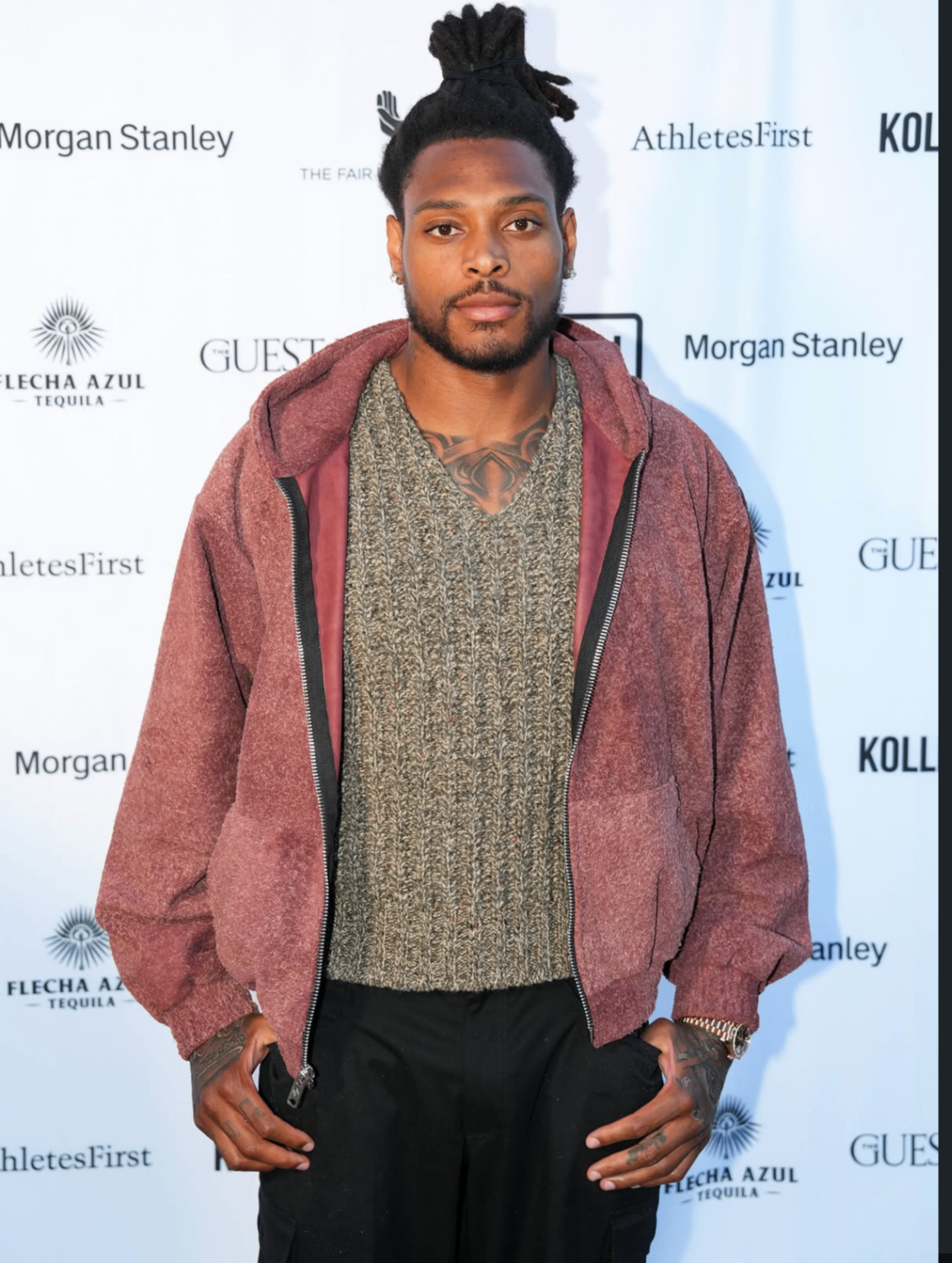 A guest in a rust suede jacket poses in front of the 2025 sponsor wall.