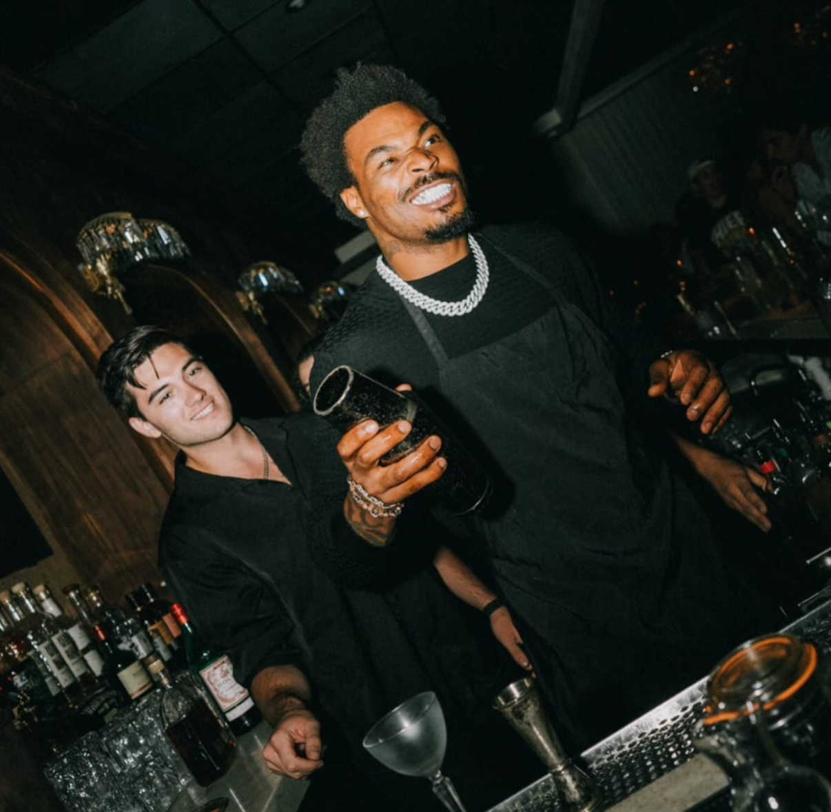Celebrity waiter and bartender share a laugh while shaking cocktails.