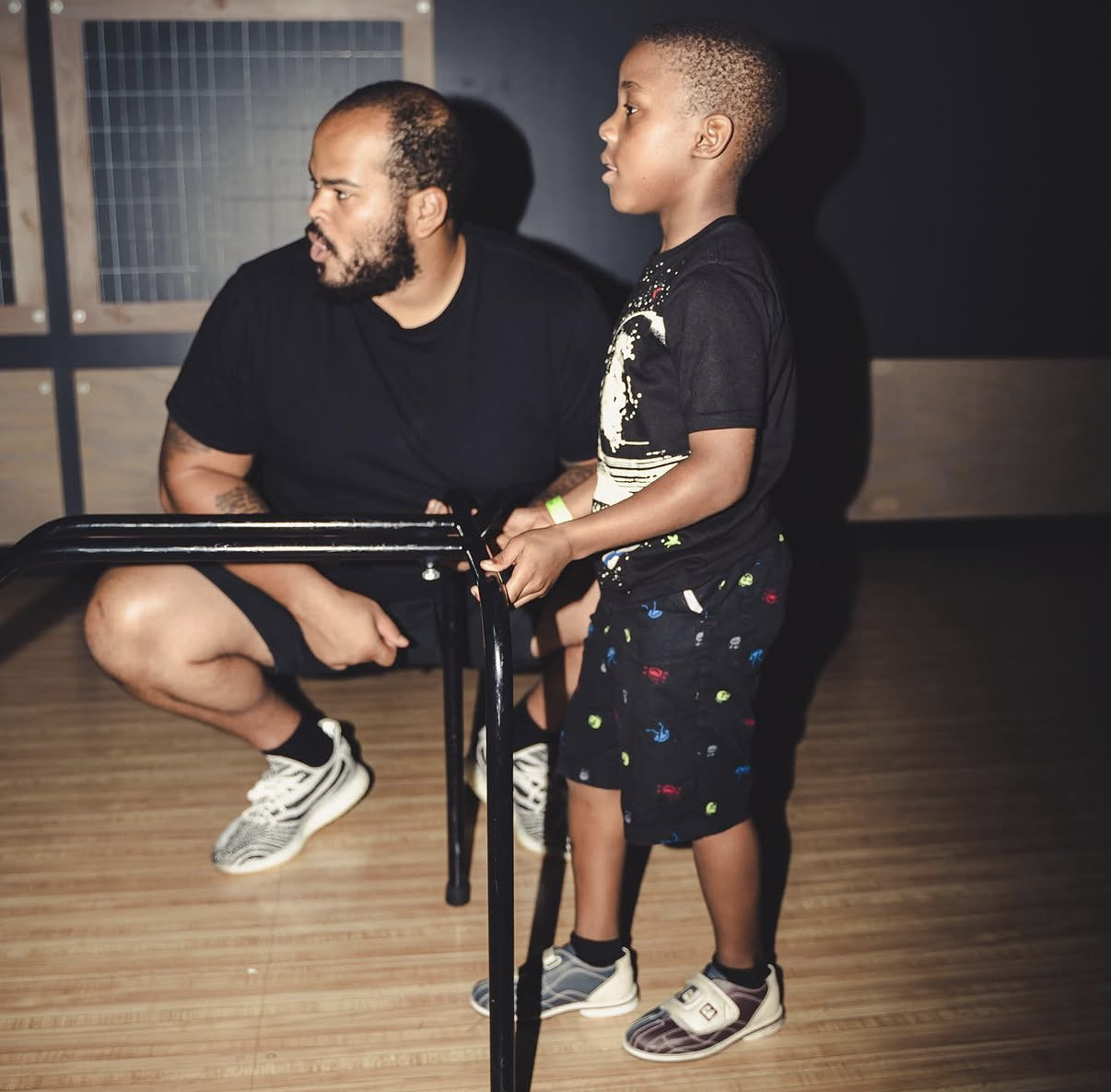 An NFL player kneels beside a young boy as they watch the lanes together at the 2019 Bowl with the Pros Charity Event.