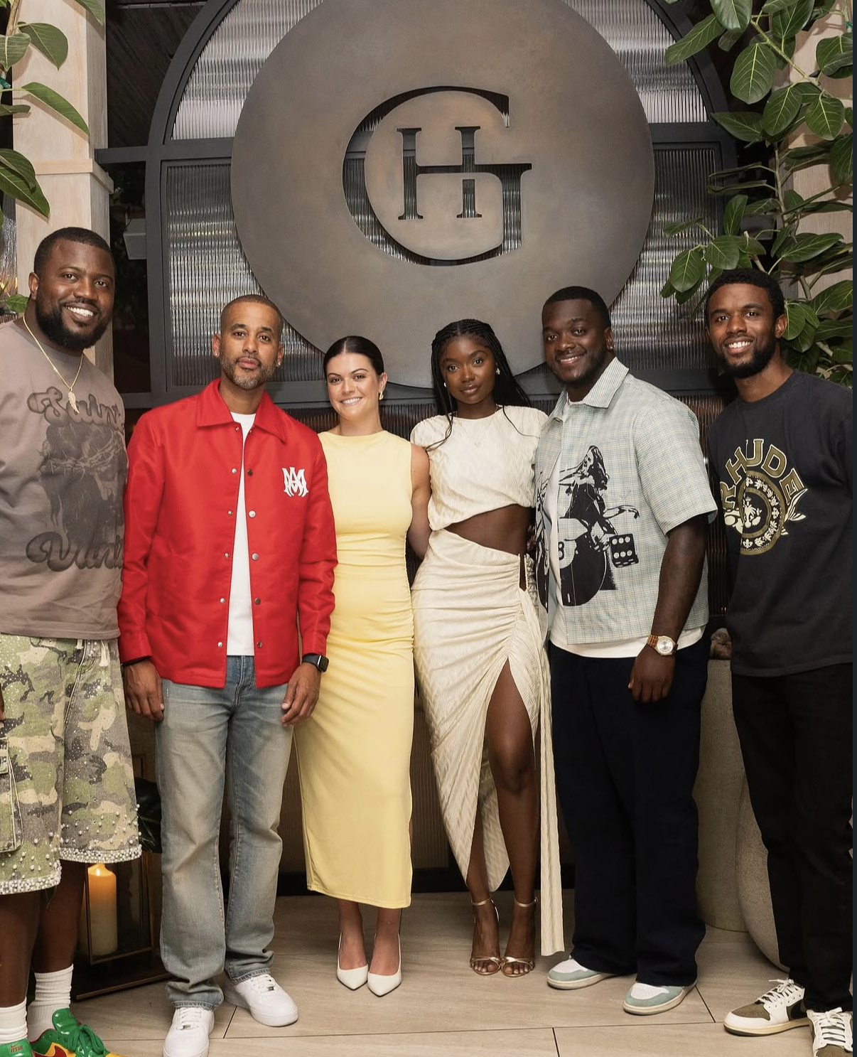 A larger group of hosts and guests pose together in front of the Guest House logo at the 2025 event.