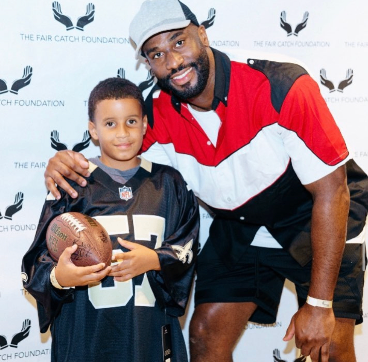 An NFL player poses with a young fan holding an autographed football at the 2018 Bowl with the Pros Charity Event.