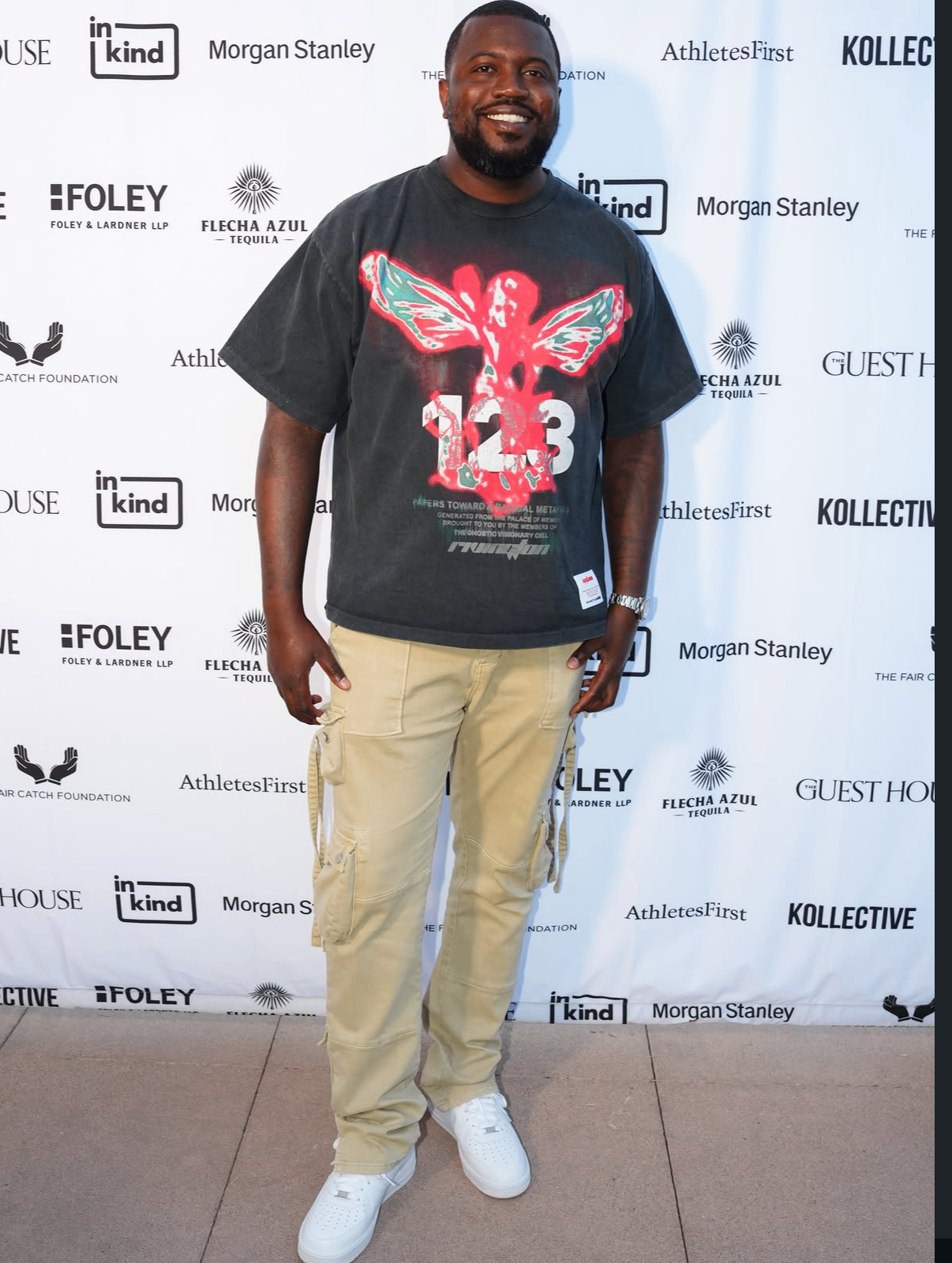 A smiling guest in a graphic tee and cargo pants on the 2025 red carpet.