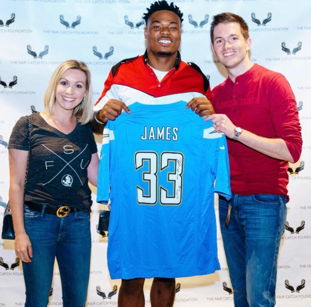 A fan poses with an NFL player holding a signed James #33 Chargers jersey at the 2018 Bowl with the Pros Charity Event.